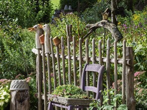 Wooden fence with duck statues and a purple chair in the garden surrounded by various plants and