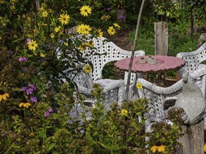 White garden furniture and yellow flowers in a quiet garden, creating a cosy corner to relax,