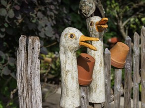 Wooden fence with decorative duck sculptures and clay pots that add a playful touch to the garden,