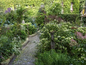 A narrow garden path leads through lush greenery and colourful flowers with an arbour of plants and