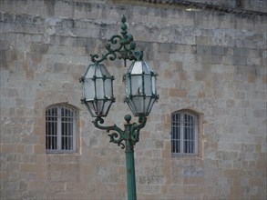 A green, artistically designed lantern in front of an old stone wall with windows, valetta,