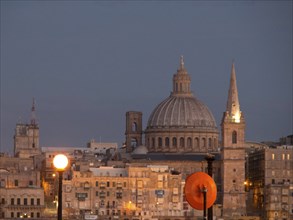 View of the dome and church tower with illuminated lanterns against the evening sky, valetta,