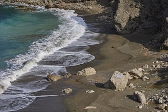Waves running over a rocky beach shore with sand and water, Atavyros beach, near Monolithos