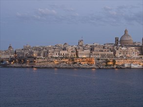 View of an illuminated town on the coast at dusk with a dome and a tower, valetta, mediterranean