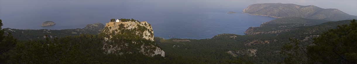 A panoramic view of a castle on a rock, surrounded by forest and coastal landscape, with the blue