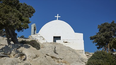 White church with a cross on a rocky hill surrounded by trees under a clear blue sky, Chapel of