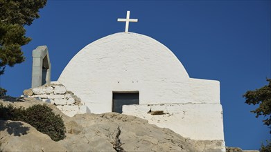 White church with a cross on a hill of rocks under a clear sky, Kastro Monolithou, Chapel of Agios