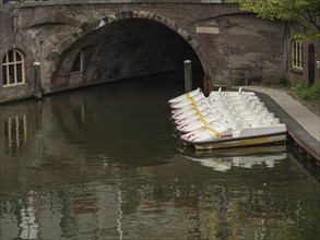 Row of pedal boats on a canal under a stone bridge in the city, utrecht, Netherlands