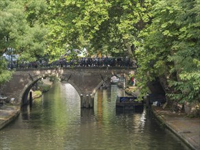 Stone bridge over quiet canal with boats and lush greenery in peaceful summer atmosphere, utrecht,