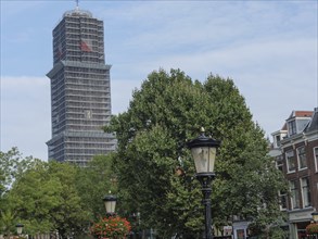 Street view with planted lanterns and a high tower with scaffolding, lined with trees and houses