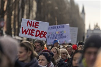 People holding signs at a manifestation in Munich. This one reads: Never Again