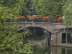 Bridge over a canal with bright flower vases and lush greenery surrounded by trees, utrecht,