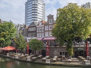 Canal landscape with rows of cafés and restaurants, lush trees and brick buildings on a sunny day,