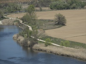 A nature shot of a winding path along a riverbank with trees and fields, toledo, spain