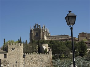 Historic castle with monumental buildings and trees, a lantern in the foreground under a blue sky,