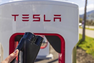 Tesla Superchargers on a parking lot, with a hand holding the CCS Type 2 plug