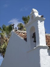 White church with a bell tower and a cross on the roof, pigeons sitting on the roof