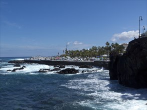 Coastal landscape with waves, cliffs and palm trees under a blue sky, Puerto de la cruz, tenerife,