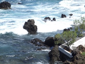 Waves crashing on the rocky shores with clear blue sea and sky, Puerto de la cruz, tenerife, spain
