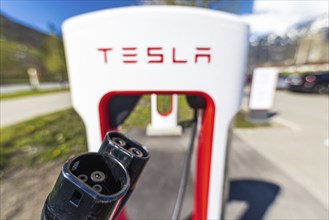 Tesla Superchargers on a parking lot, with a hand holding the CCS Type 2 plug