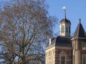 Close-up of a castle tower with a weather vane and large trees in the background, ruurlo,