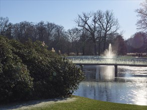 A fountain in the park, surrounded by water and bare trees in the winter sunlight, ruurlo,