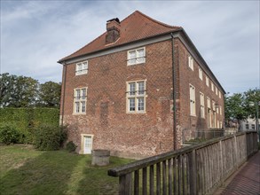 Brick building with gable roof and chimney, surrounded by a green meadow and a wooden fence,