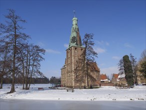 A castle with a tower in a snow-covered park with trees and historical architecture under a clear