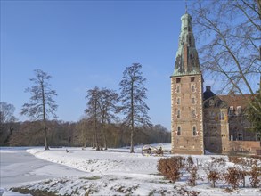 A castle with a tower in a wintry, snow- and tree-covered park landscape under a clear sky,