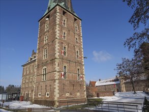 Large brick castle with tower, surrounded by snow and blue sky, typical winter atmosphere,