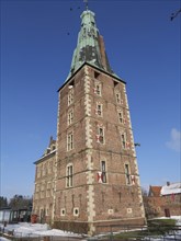 A high brick tower of the castle in winter with snow-covered ground and blue sky, Raesfeld,