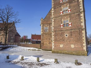 A historic brick castle covered in snow, surrounded by trees under a blue sky, Raesfeld,