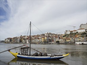 A boat with wine barrels floats on a river in front of a historic city, Porto, Douro, Portugal,