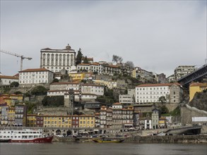 Riverside buildings stretch up the slopes of a hill, with overhanging cloud cover, Porto, Douro,