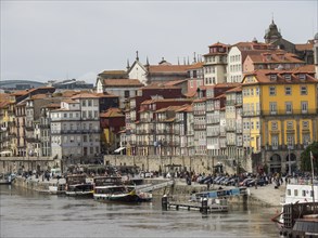 Coastal view of a city with colourful buildings, river, boats and people on the shore, Porto,