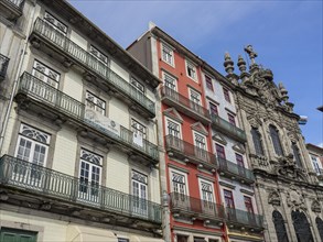Row of buildings with balconies and windows next to a historic church under a blue sky, Porto,