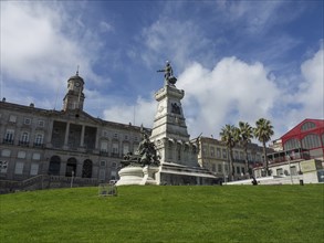 Monument on a green square in front of magnificent historical buildings and palm trees, Porto,