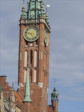Close-up of a high church tower with clock, built of bricks, in front of a cloudy sky, Gdansk,