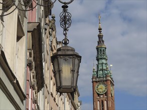 Old lantern in front of historic buildings and a tall church tower with a clock in the background,