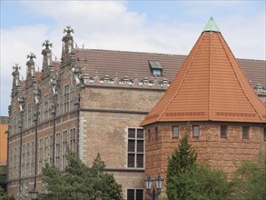 A historic building with red tiled roofs and a bay tower, surrounded by trees, Gdansk, Poland,