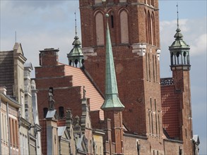 A Gothic church tower made of red bricks with stone statues on nearby historic buildings, Gdansk,