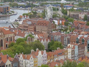 Bird's eye view of a city with a Ferris wheel on the river, surrounded by colourful houses and