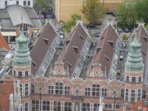A historic building with ornate copper towers and skylights in a bustling city centre, Gdansk,