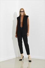 Stylish professional woman in chic black vest, terracotta sweater and tailored trousers, standing