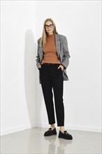 Stylish woman wearing checkered blazer and brown turtle neck sweater and black trousers standing