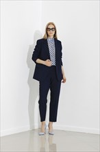 Professional woman stands confidently against a white wall, dressed in a chic navy blue business