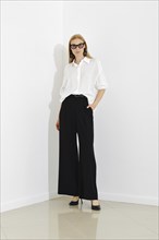 Stylish modern woman in loose black trousers and white shirt paired with glasses and leather