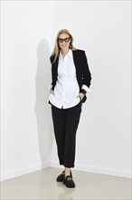 Slim beautiful blonde business woman standing near white office wall in casual black suit. Concept