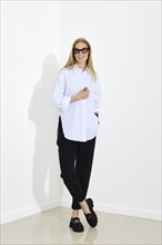 Urban-style fashion portrait of happy smiling woman wearing white shirt and black trousers.
