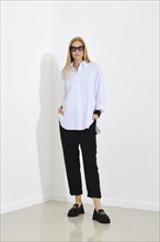 Blonde woman posing in white button down cotton shirt and loose trousers